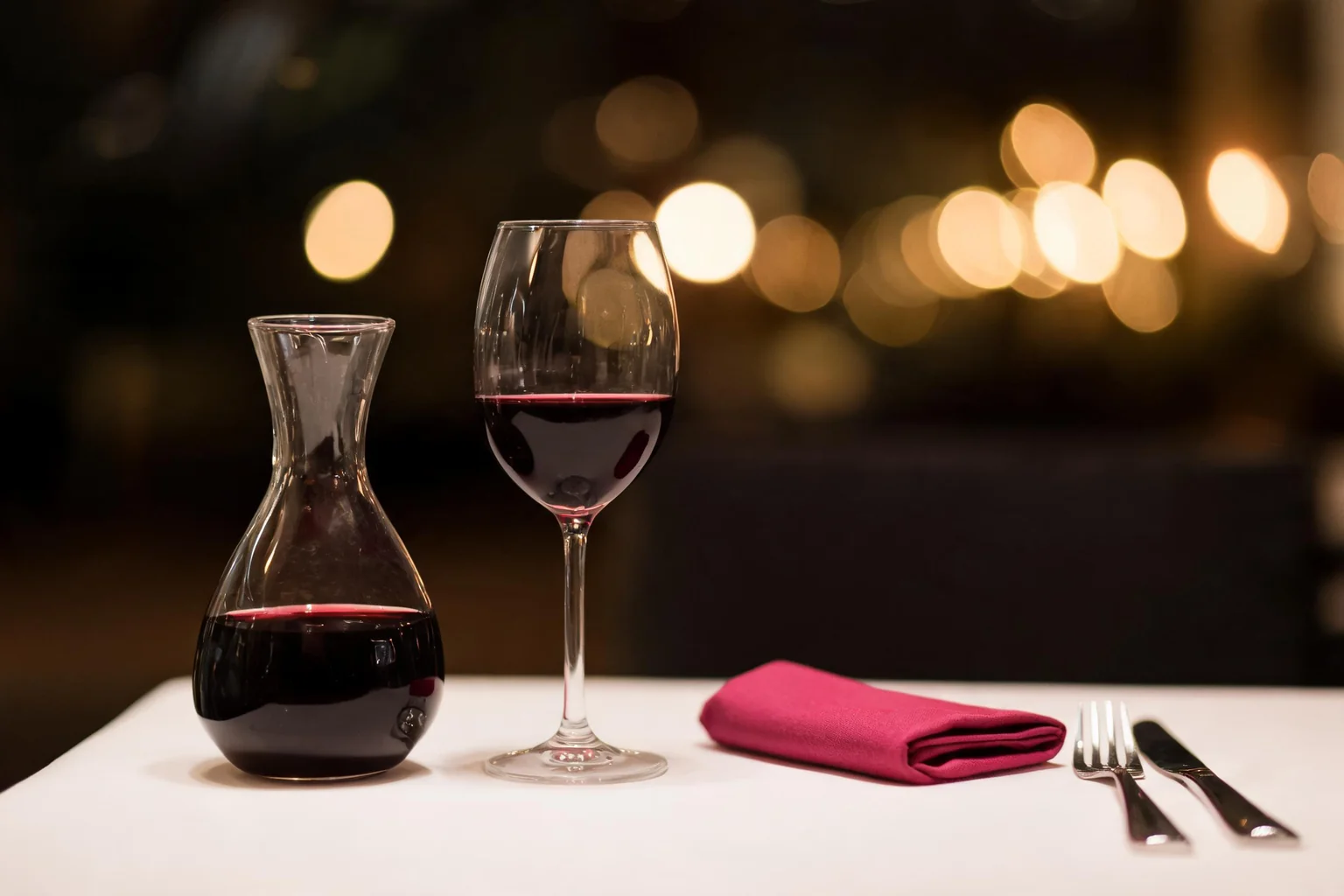 Carafe and glass of red wine on a white table, fuchsia napkin